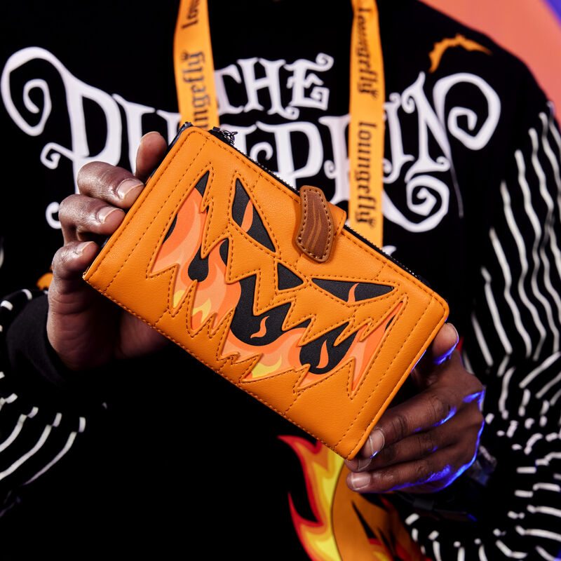 Man holding the Nightmare Before Christmas Jack Pumpkin Head wallet toward camera, featuring a jack-o'-lantern face on fire